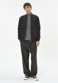 Tume bomberjakk sileda pinnaga, halli soonikkoega kõrge kaelusega kampsun, lõdvalt istuvad pruunid püksid ning mustad tossud valgete detailidega.