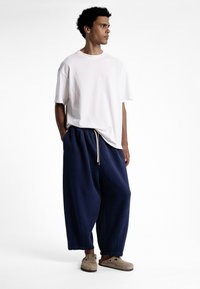 T-shirt blanc surdimensionné, pantalon large marine avec cordon de serrage, et sabots marron clair. Matériaux simples et confortables avec une coupe décontractée.