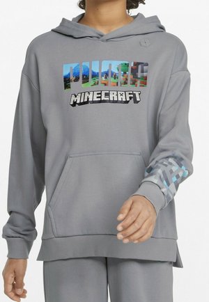 Personne portant un sweat à capuche gris Minecraft avec un graphique coloré "PULSE" et un design pixellisé sur le bord de la manche droite.