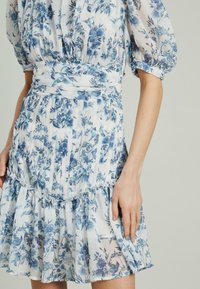 Abito con fantasia floreale in tessuto leggero e arioso, nei colori blu e bianco. Presenta maniche a sbuffo, una vita stretta e un orlo arricciato.