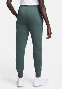 Gröna, smala träningsbyxor i mjukt material. Har resår i midjan, sidofickor och ribbstickade muddar. Matchas med vita sneakers.