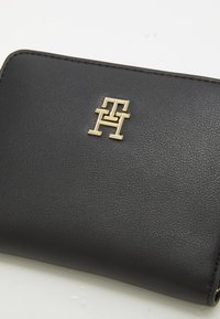 Schwarze Lederbörse mit strukturierter Oberfläche. Verfügt über ein goldenes Logo-Element und sauber genähte Kanten. Kompakte rechteckige Form.