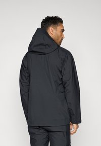 Giacca impermeabile nera con cappuccio, caratterizzata da una vestibilità comoda, una texture liscia e dettagli di cuciture sottili. Vista posteriore che mostra la lunghezza e le linee del design.