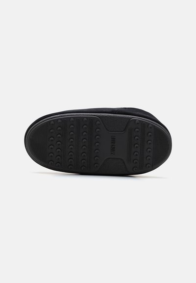 Zwarte schoenen met een gestructureerde rubberen zool met cirkelvormige grippatronen en een gladde zijafwerking. Het ontwerp is laag profiel en minimalistisch.