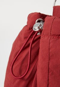 Tessuto rosso con una leggera texture stropicciata, con un fermo in argento dotato di un anello per il laccio. Cuciture decorative lungo il bordo.