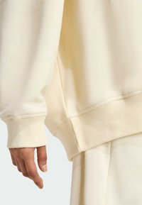 Sudadera de gran tamaño en color beige claro, con puños acanalados y tejido texturizado. Corte holgado con detalles de costura visibles.