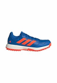Chaussure de sport bleue avec des rayures orange et des crampons sous la semelle, conçue pour les sports en plein air ou la course sur sentier.