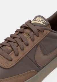 Close-up of brown Nike sneaker with textured laces, suede and leather panels, and visible Nike logo on the side and tongue.