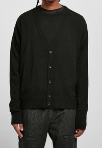 Czarny dzianinowy kardigan z dekoltem w kształcie litery V, długimi rękawami i guzikami z przodu. Posiada strukturalny materiał oraz żebrowane mankiety i dół.