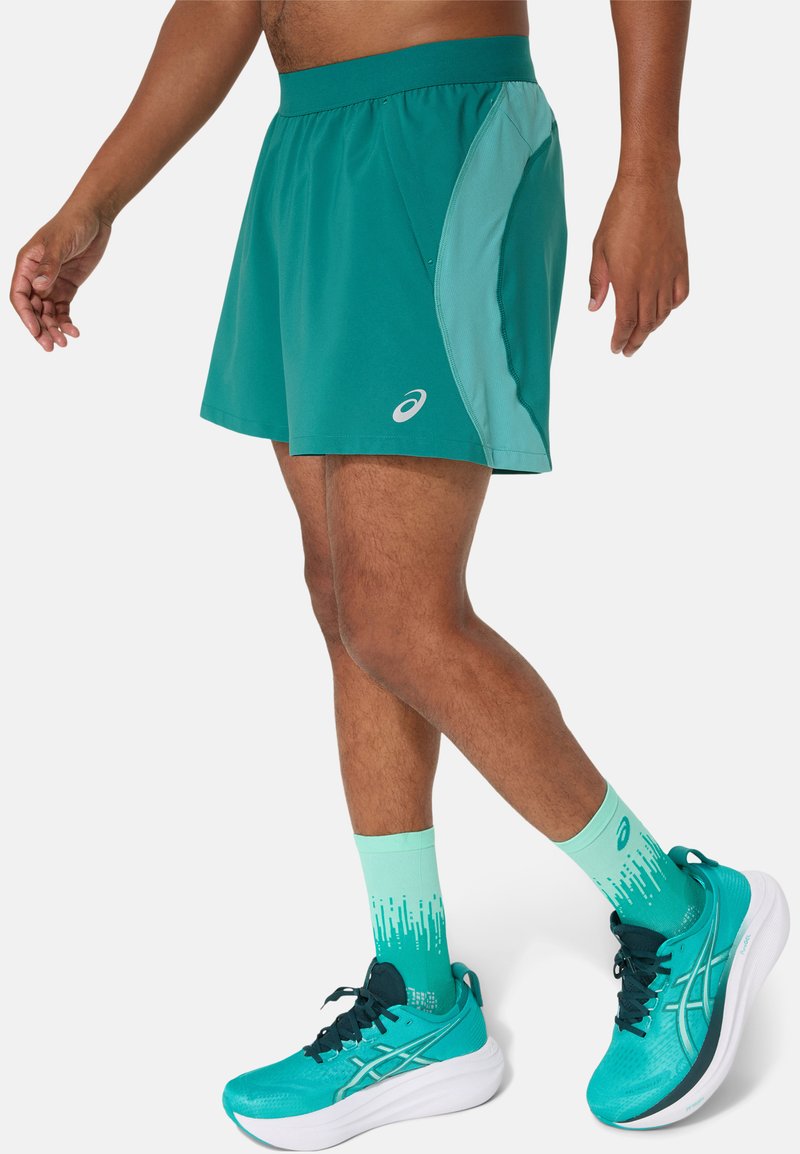 Turquoise sportshorts met een contrasterend lichtgroen zijpaneel, met een zachte textuur en een logo aan de onderzijde aan de voorkant.