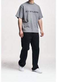 Szary bawełniany t-shirt z czarnym nadrukiem „2Y STUDIOS”, zestawiony z czarnymi spodniami typu cargo i białymi sneakersami, o luźnym kroju.