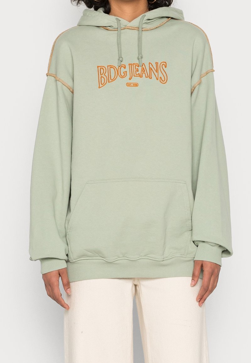 Sudadera verde claro con un bolsillo tipo canguro, puños acanalados, texto en naranja "BDG JEANS" en contraste y capucha con cordón. Material de algodón suave.
