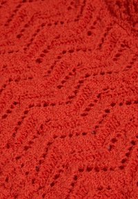 Strukturierter roter Stoff mit einem Zickzackmuster und kleinen Öffnungen, der eine weiche, geschlungene Oberfläche aufweist, die die taktile Qualität verbessert.