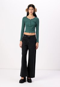 Mørkegrønn ribbet langermet topp med henley-hals, sammen med høyt liv og vide svarte jeans og klumpete plattform sko.