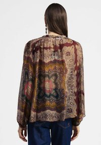 Blusa trasparente a maniche lunghe con un motivo paisley in colori caldi. Collo rotondo, dettagli arricciati sul retro e polsini elastici.