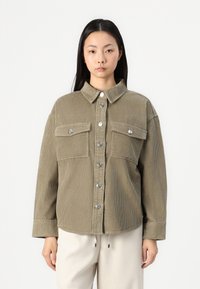 Chemise en velours côtelé vert olive, avec un devant �à boutons, deux poches poitrine et des boutons-pression en métal argenté. Silhouette boxy avec manches à revers.