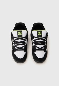 Svarta och vita sportskor med en texturerad yta, med snörningsdesign, vadderad krage och en grön logotyp på tungan.