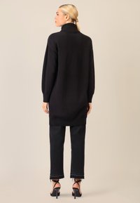 Schwarzer Rollkragenpullover mit lockerer Passform, langen Ärmeln und geripptem Saum, kombiniert mit schwarzen, cropped Jeans und Riemchen-Heels.