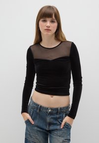 Zwarte top met lange mouwen met een doorschijnend mesh bovenpaneel, een getailleerd ontwerp en zacht materiaal; gecombineerd met lichtgewassen denim cargobroek.