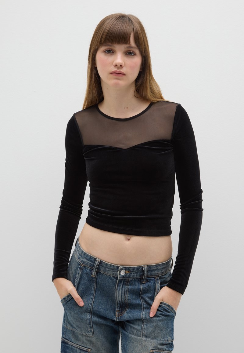 Zwarte top met lange mouwen met een doorschijnend mesh bovenpaneel, een getailleerd ontwerp en zacht materiaal; gecombineerd met lichtgewassen denim cargobroek.