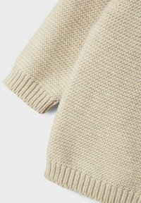 Maglione lavorato a maglia beige con un motivo testurizzato, caratterizzato da polsini e orlo a coste. Materiale morbido con un design ampio.