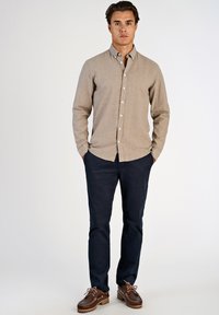 Camicia beige con bottoni e maniche lunghe, abbinata a pantaloni blu navy e scarpe stringate marroni. La camicia presenta una trama sottile e un colletto standard.