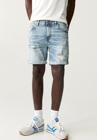 Light wash denim shorts with distressed details and rolled cuffs, paired with gray and blue athletic shoes and white crew socks.
