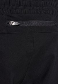 Czarne spodnie z teksturowanym elastycznym paskiem w talii oraz bezpieczną kieszenią zapinaną na zamek, wykonane z gładkiego materiału z wyraźnymi detalami szycia.