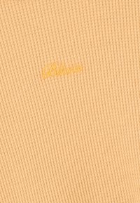 Svijetlosmeđi rebrasti materijal s utisnutim "Blvck" logotipom u žutoj boji, prikazujući teksturirani, mekani materijal s suptilnim detaljima.