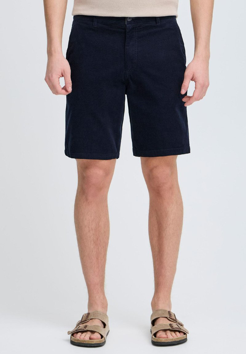 Mørkeblå bomullsshorts med frontlommer, knappelukking og rett passform, kombinert med brune sandaler med to stropper.