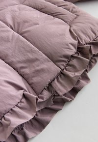 Purple, puffy quilt with a soft, textured surface and ruffled edges, folded to showcase its fullness and design details.
