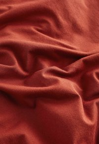 Tissu de couleur rouille avec une texture douce et lisse, présentant de légers plis et plis. Idéal pour des applications vestimentaires ou de tapisserie.