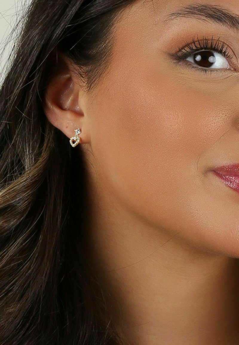 Guldtonade hjärtformade örhängen med en klar ädelsten som accent, som visar en polerad yta och intrikata design detaljer.