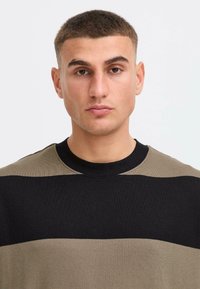 Pull rayé vert foncé et noir avec un col rond et une texture côtelée, présentant un design simple et moderne.