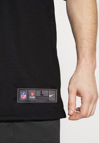 Czarna koszulka sportowa z logo NFL i Nike na metce. Materiał jest lekki o gładkiej fakturze, skrojona na luźny krój.