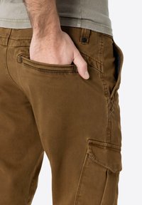 Brown cargo pants displaying a smooth fabric texture, side pocket, and a fitted design with a button closure at the waistband.