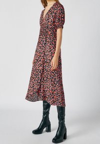 Vestido midi negro con estampado floral en tonos rosa y naranja, con mangas cortas abullonadas, escote en V profundo, combinado con botas negras de tacón alto.
