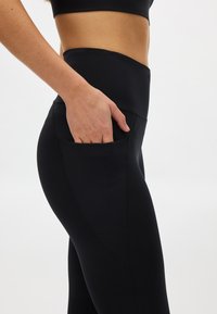 Zwarte legging met hoge taille gemaakt van rekbaar materiaal, voorzien van een zijzak en een glad oppervlak, met flatlocknaden voor comfort.