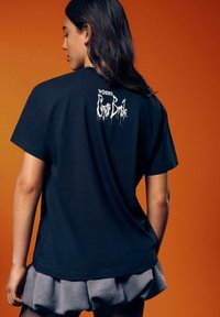 Schwarzes, übergroßes T-Shirt mit weißem Text „Tim Burtons Corpse Bride“ auf dem Rücken. Weicher Stoff, kurze Ärmel, lässige Passform.