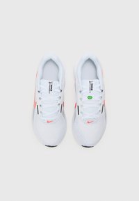 Scarpe da ginnastica bianche con tessuto in rete, dettagli neri e Swoosh arancione. Presentano sei passanti per i lacci e una suola bianca texturizzata. Etichetta verde attaccata.