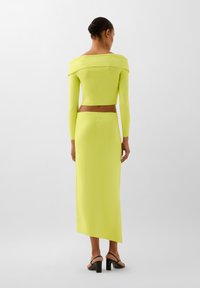 Completo a due pezzi di un vivace giallo neon, con top corto a spalle scoperte e una gonna lunga fino al pavimento con uno spacco laterale.