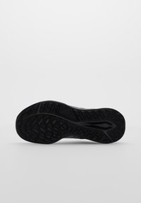 Black athletic shoe sole with a textured rubber pattern, featuring grooves and raised sections for grip and stability.