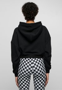 Svart avkortet hettegensere med stor hette, kombinert med rutete leggings i svart og hvitt, med en tettsittende design og glatt tekstur.