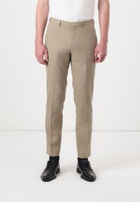 Beige tailored trousers with a flat front, slim fit design, and subtle texture. Paired with black dress shoes, standing against a light background.