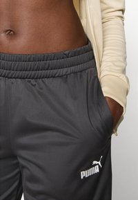 PUMA sports pants in dark gray, featuring a soft texture, elastic waistband, and a white logo on the left pocket area.