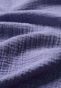 Tessuto texturizzato viola con un aspetto ondulato, caratterizzato da un sottile motivo di pieghe che ne esalta la qualità tattile.