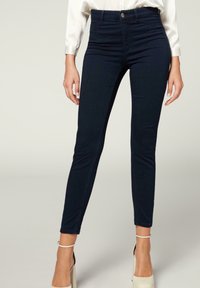 Jeans de talle alto en color navy con corte ajustado, confeccionados en denim elástico. Cuentan con un cierre frontal de botón y bolsillos. Textura suave.