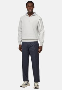 Felpa grigia chiara con metà zip e tasca a marsupio, abbinata a pantaloni navy e sneakers crema con dettagli blu.