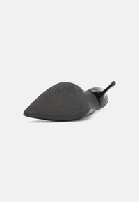 Zwarte puntige stiletto-hak getoond vanaf de onderkant, met een getextureerde rubberen zool en een glanzende lakafwerking.