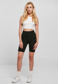 Svart sykkelshorts med høyt liv og glatt tekstur, kombinert med en hvit ermeløs crop top. Brukes med hvite joggesko og ankelsokker.